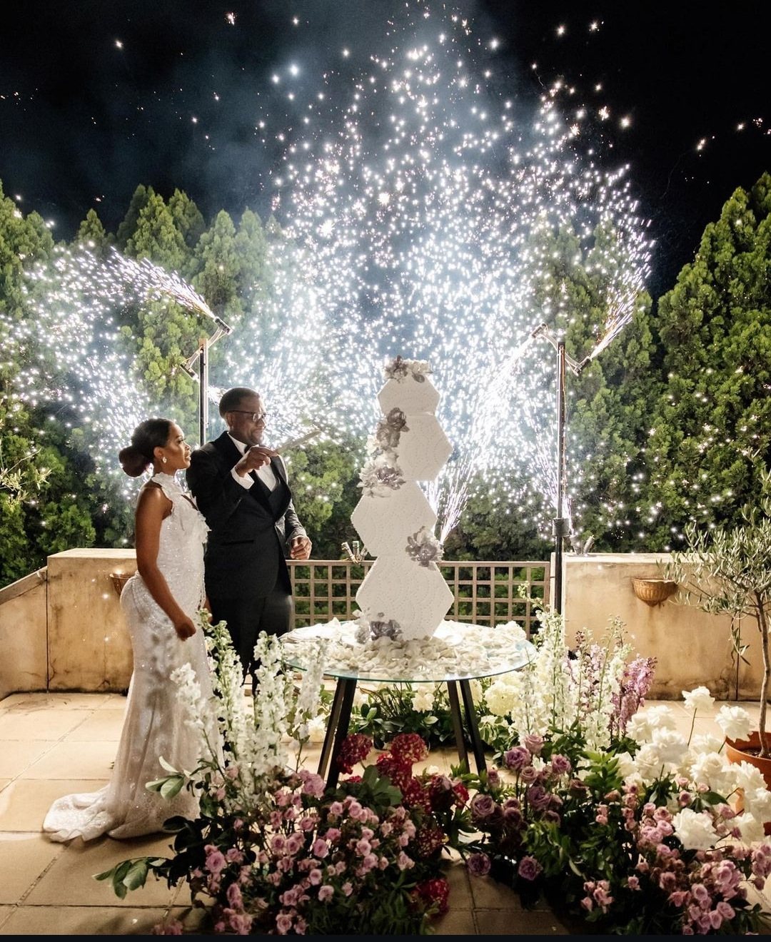 Couple at a wedding with a cake and pyrotechnics in background.