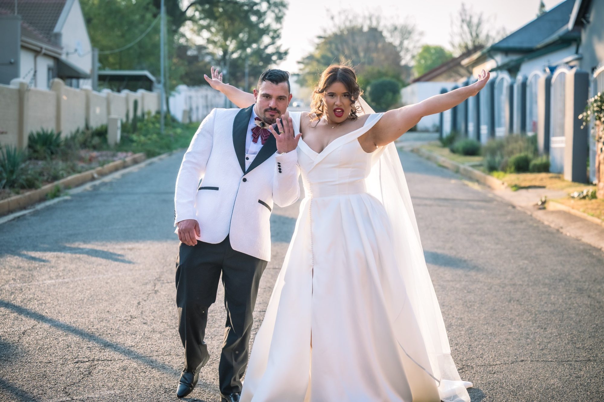 Couple in wedding attire posing playfully on a street