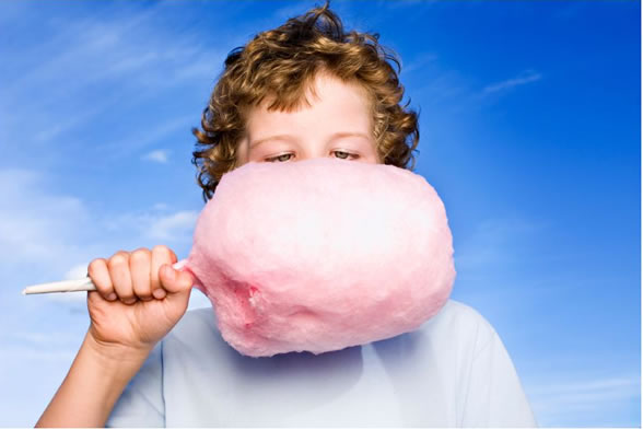 Boy holding pink cotton candy against blue sky