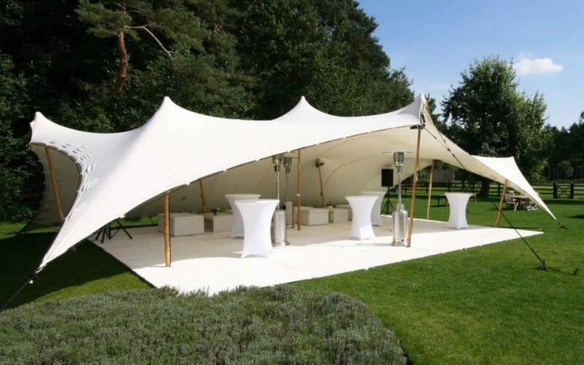 White stretch tent set up on a lawn with cocktail tables