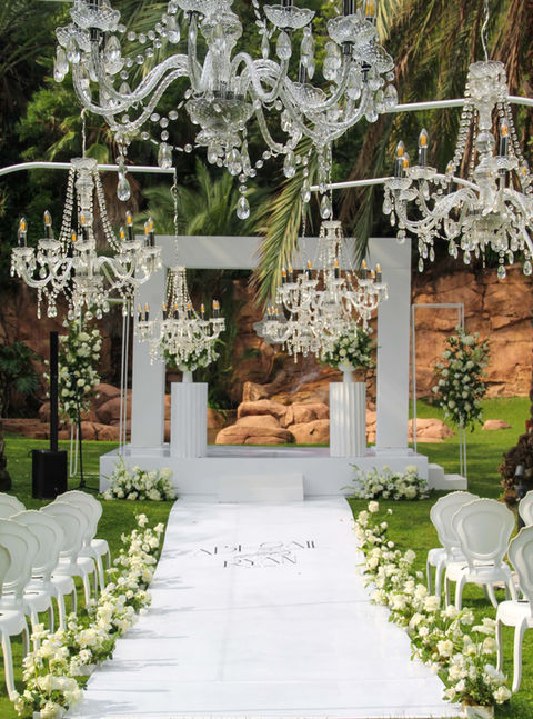 Outdoor wedding setup with chandeliers and floral arrangements