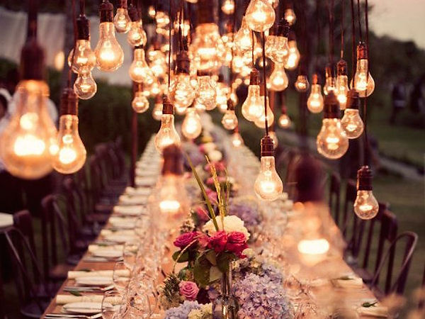 Long dining table with hanging Edison bulbs and floral arrangements