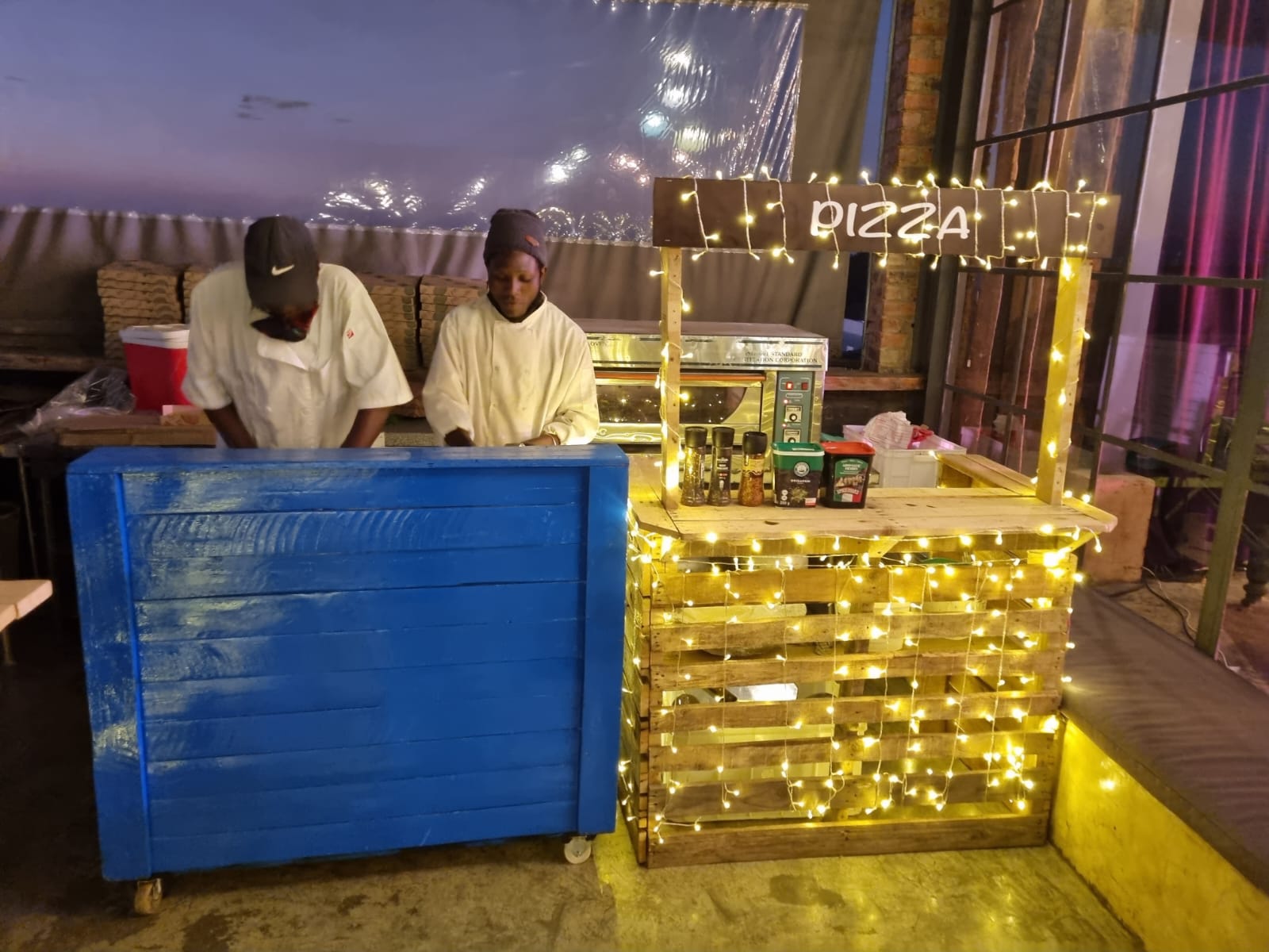 Pizza station with staff preparing pizzas and decorative lighting.