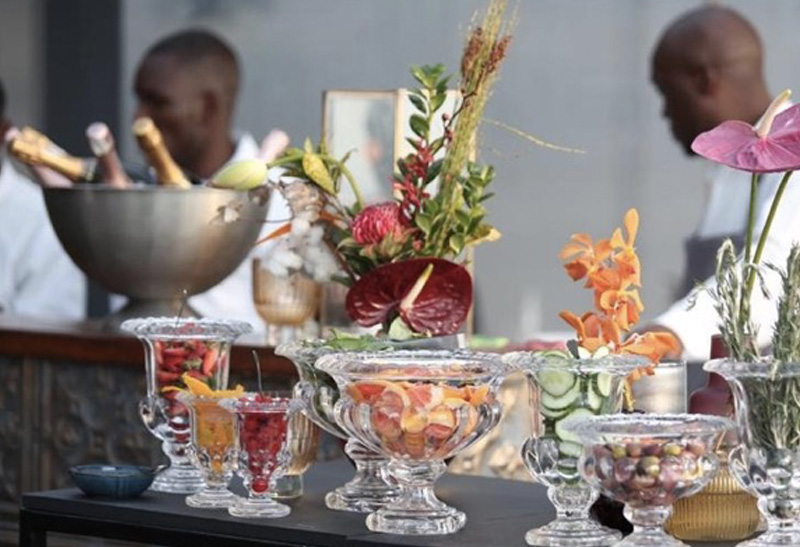 A decorative beverage station with fruit garnishes and floral elements