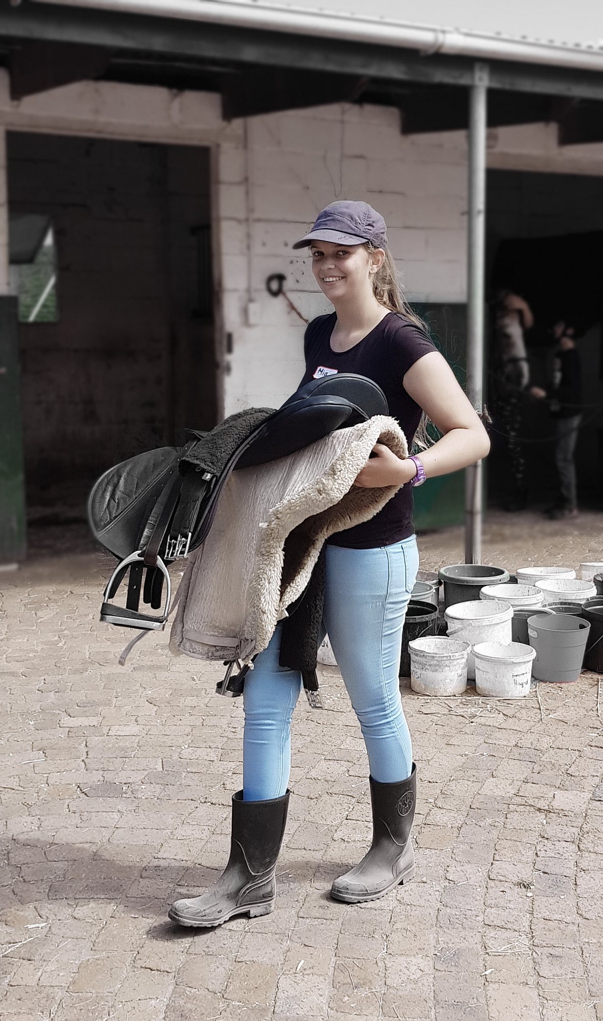 A staff member carrying saddlery in a stable area.