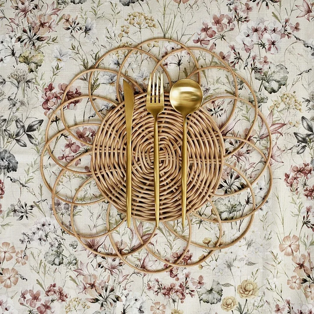 Wicker charger with gold fork and spoon on floral tablecloth.