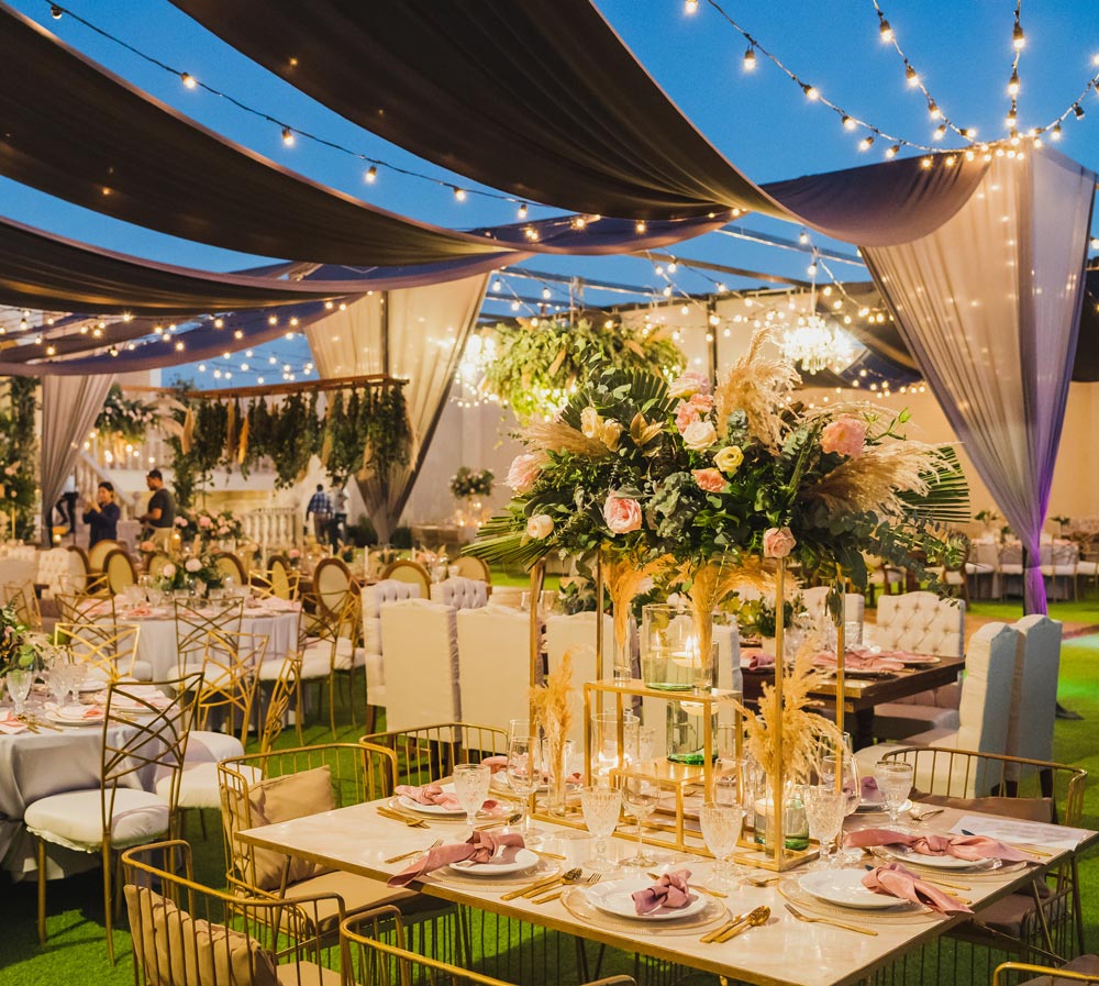 Elegant outdoor event setup with tables, flowers, and string lights.
