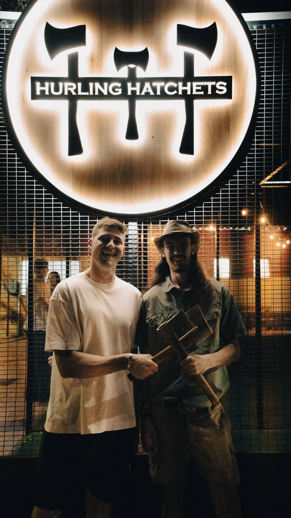 Two men holding axes in front of Hurling Hatchets sign.