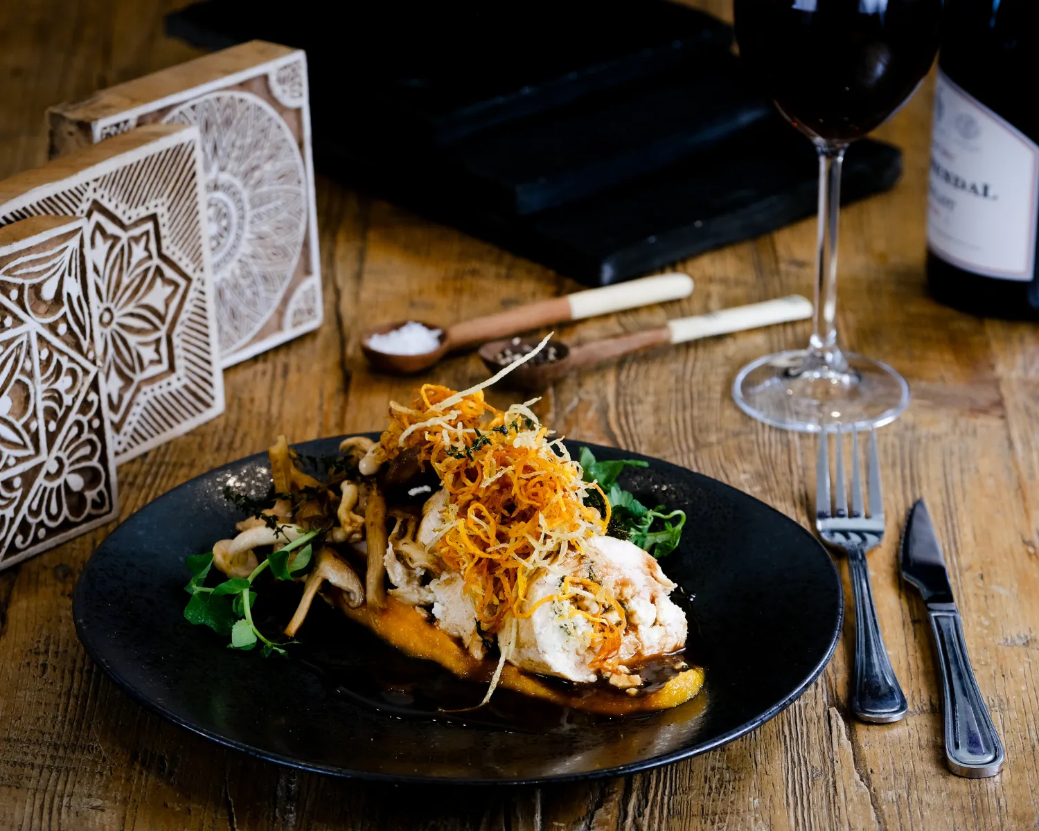 Plated chicken dish with mushrooms and crispy garnish on a wooden table.