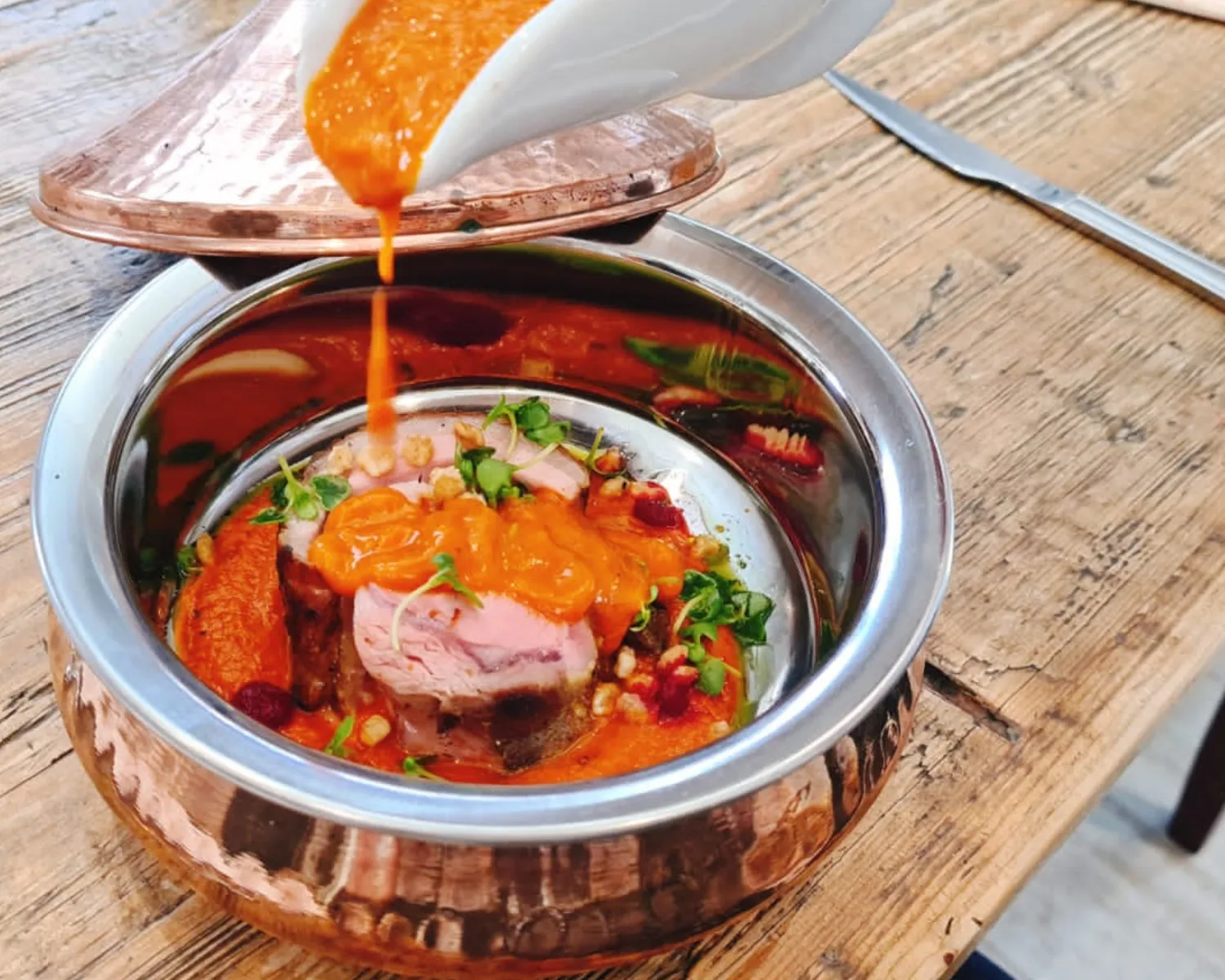 Chef pouring sauce over gourmet dish in copper bowl