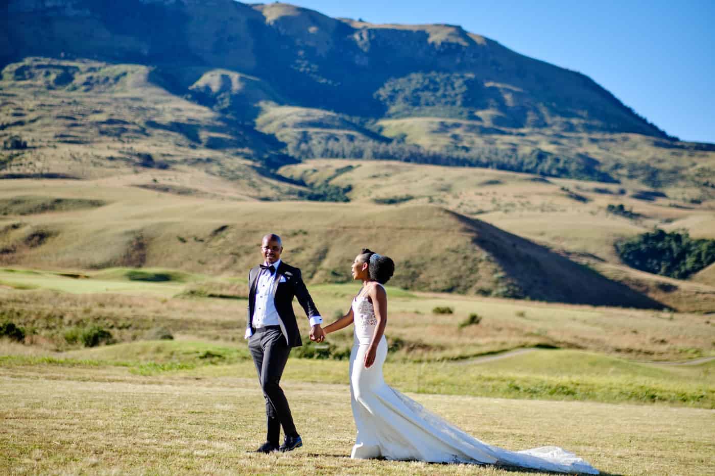 Bride and groom walking hand-in-hand in a scenic outdoor setting.