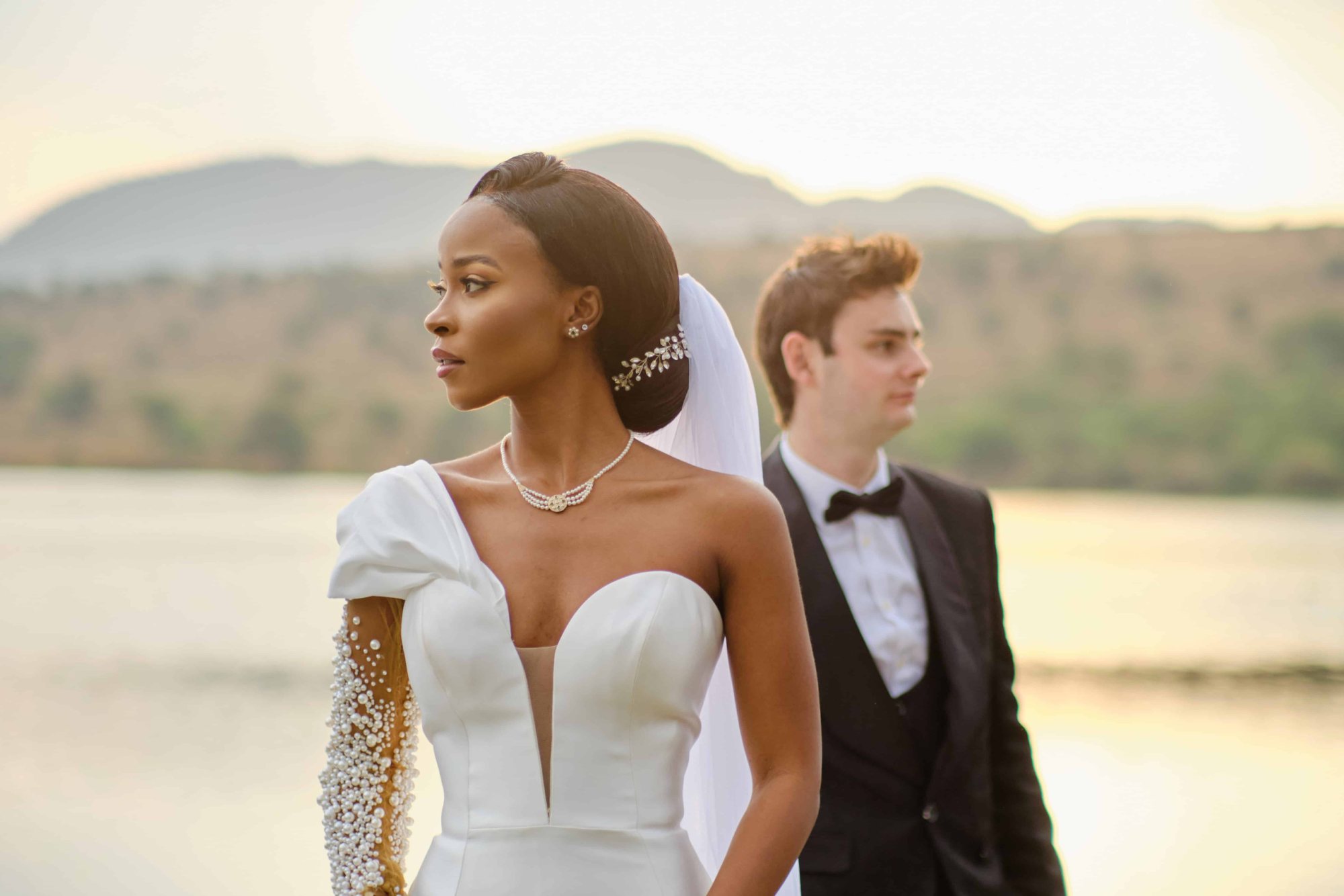 Bride in white gown and groom at sunset by a lake.