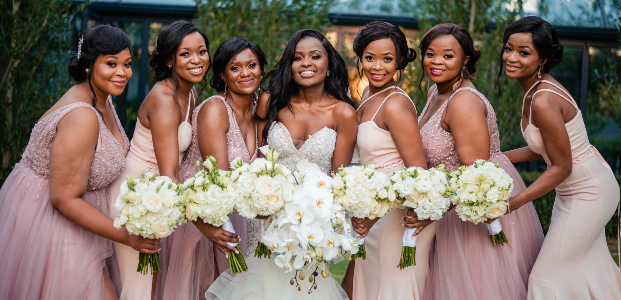 Bride and bridesmaids with bouquets in a garden setting.