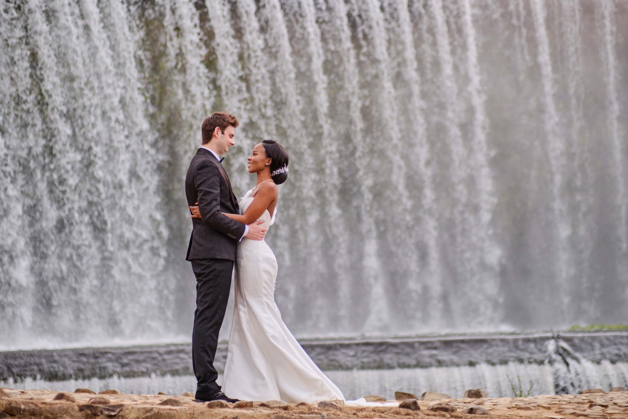 Bride and groom embrace near a waterfall.