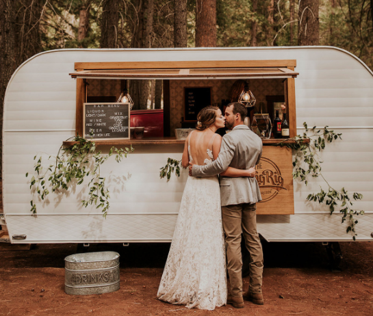 Mobile bar with two people in front, surrounded by trees