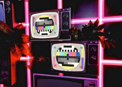 Retro TVs with colorful test screens against neon backdrop.