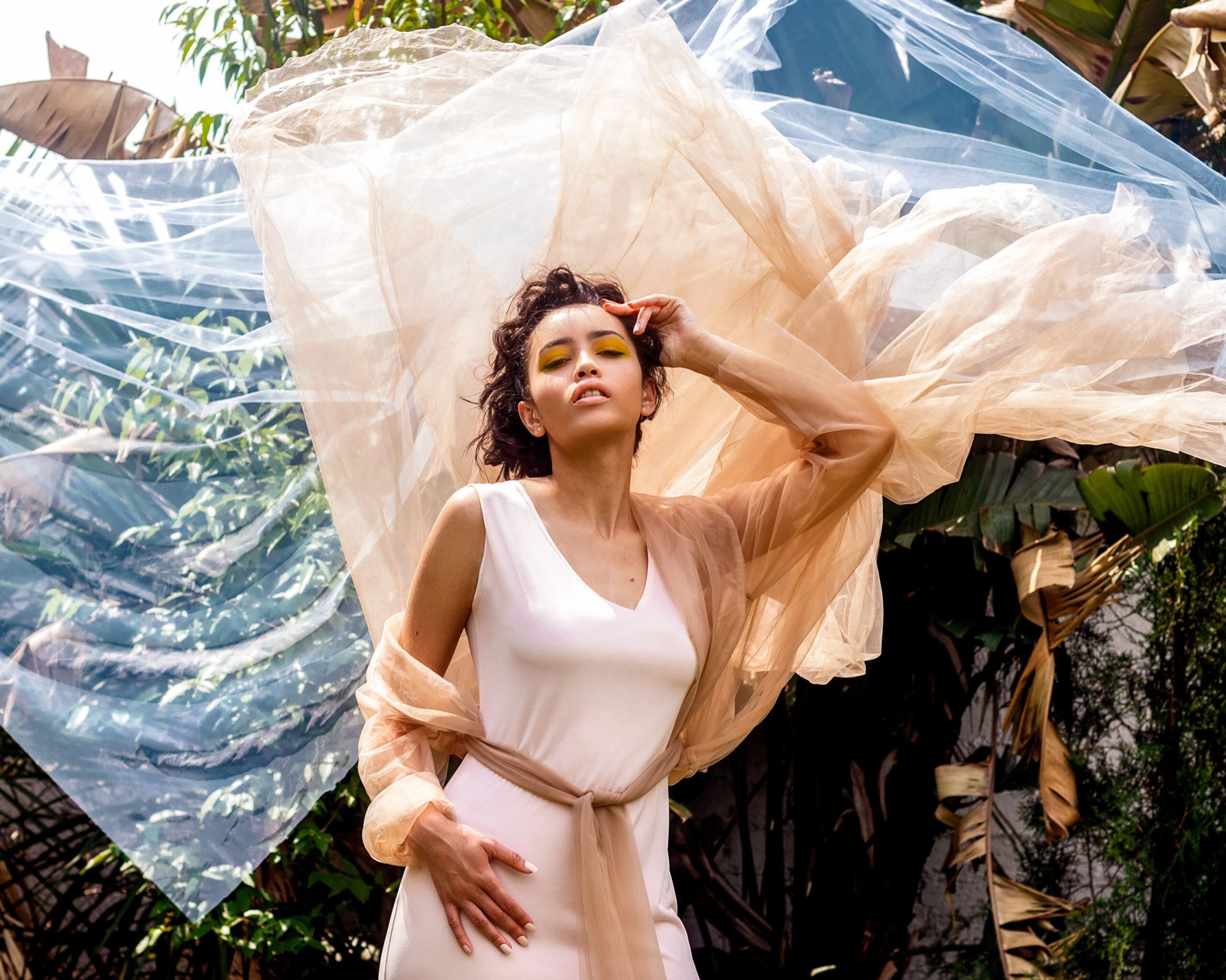 Model posing in airy fabric with greenery behind