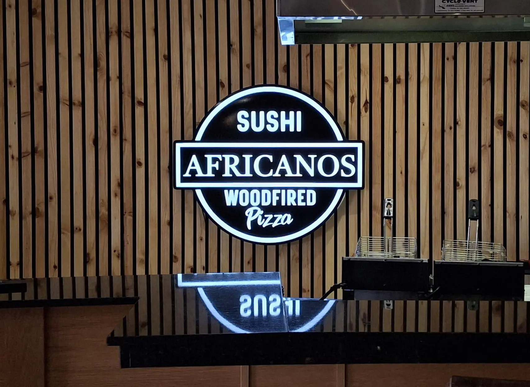 Neon sign for Africanos showing Sushi and Woodfired Pizza