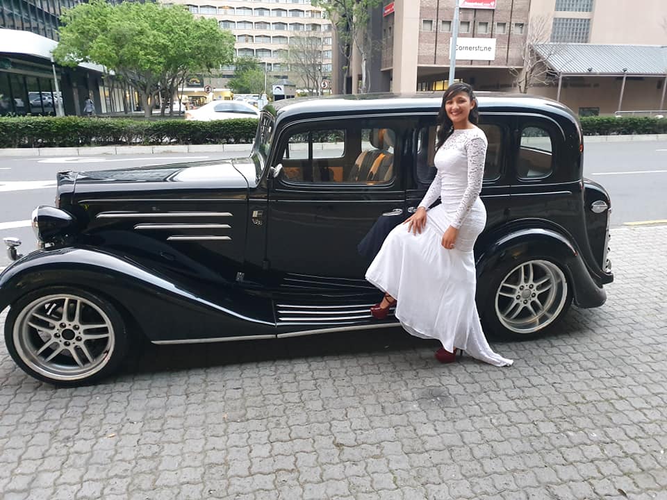 A woman in a white dress beside a vintage car