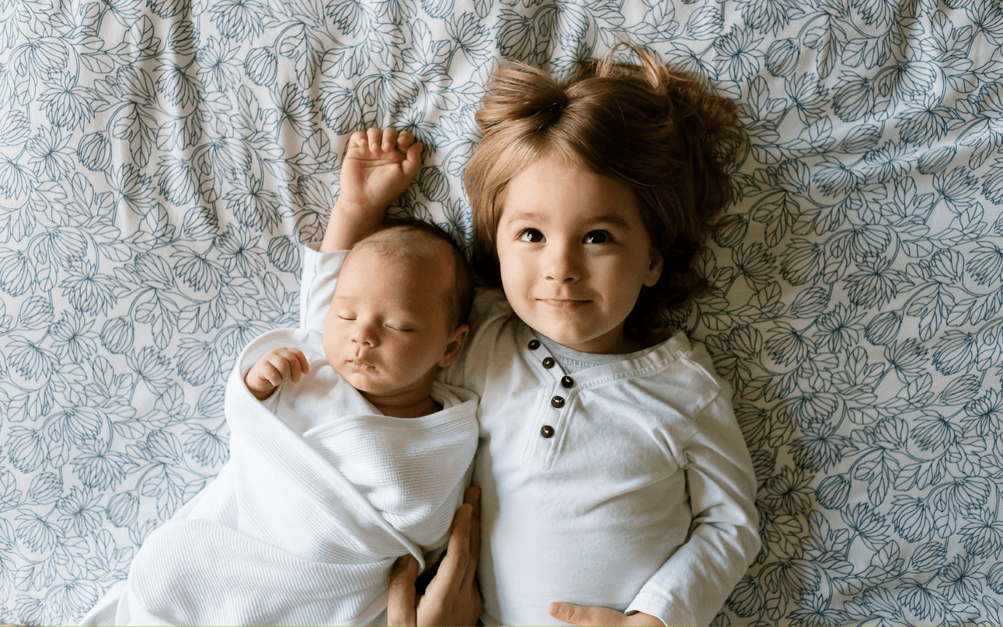 A child and an infant lying on a patterned blanket.