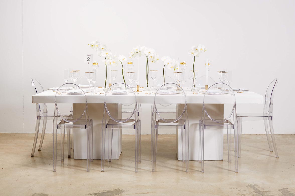 Elegant dining table with transparent chairs and floral arrangements.