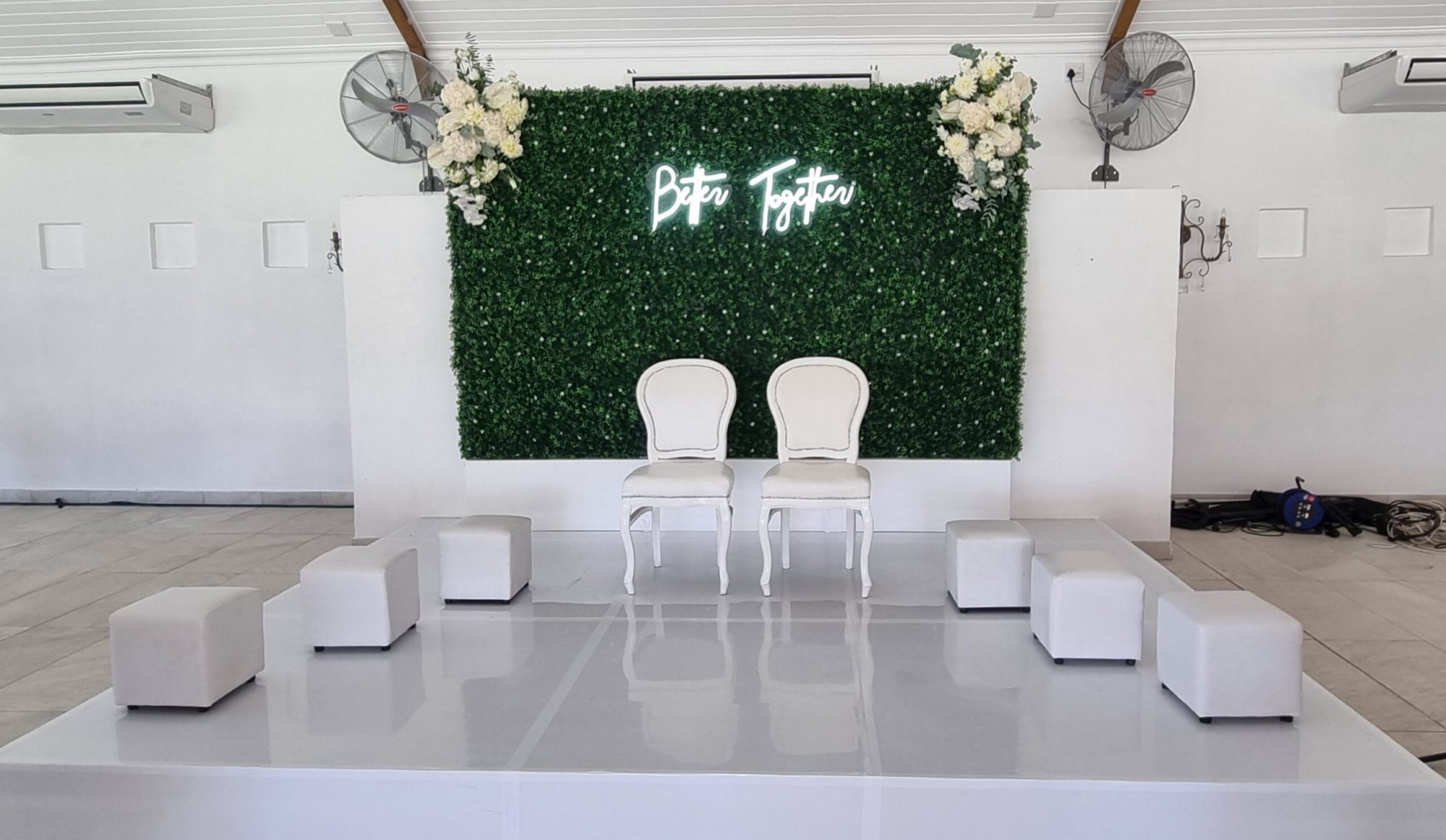 Event stage with greenery backdrop and white chairs
