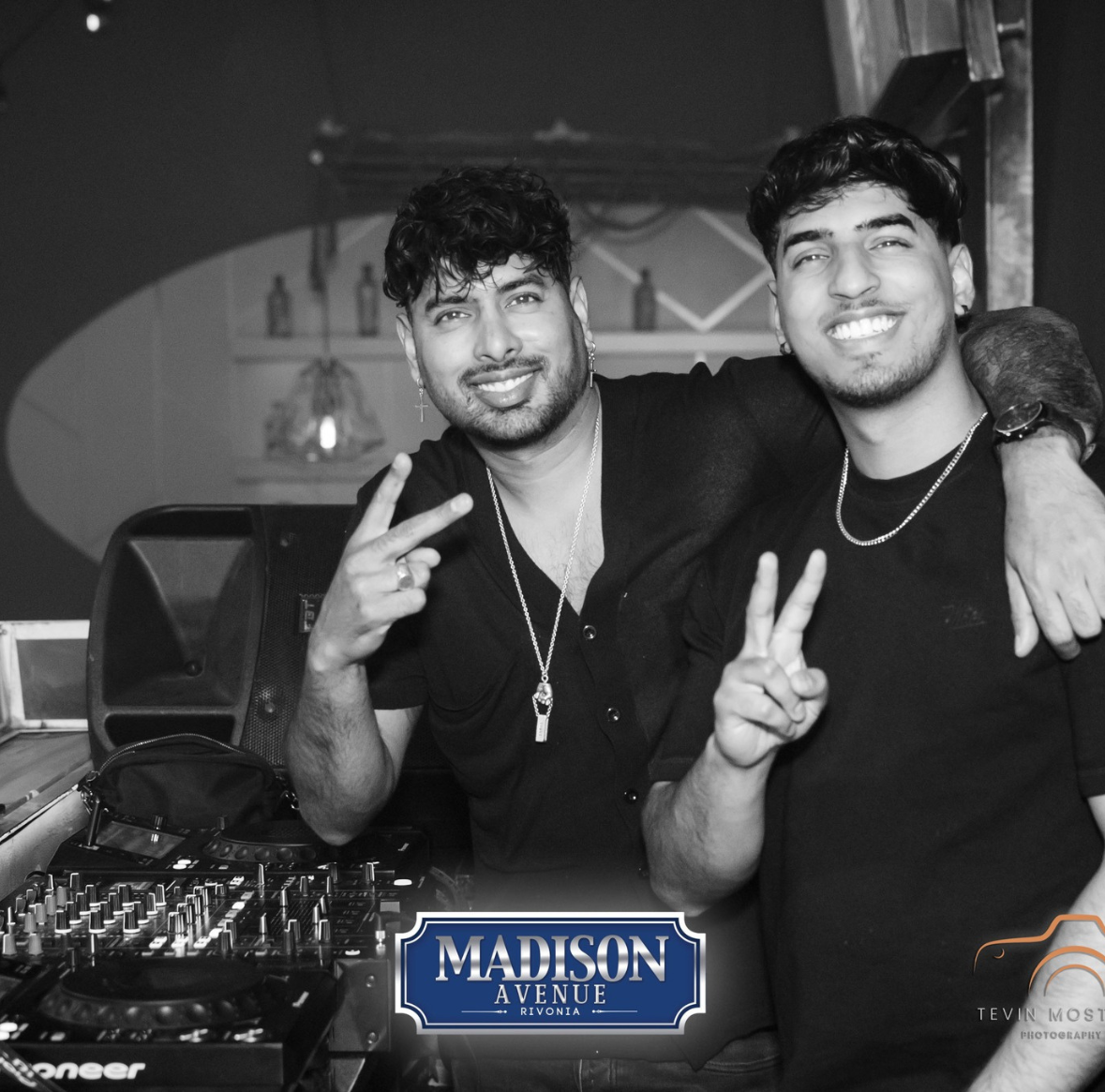 Two DJs smiling and posing behind a DJ booth at Madison Avenue Rivonia.