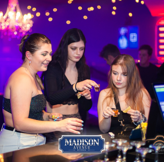 Three women enjoying drinks at the bar in a nightclub setting.