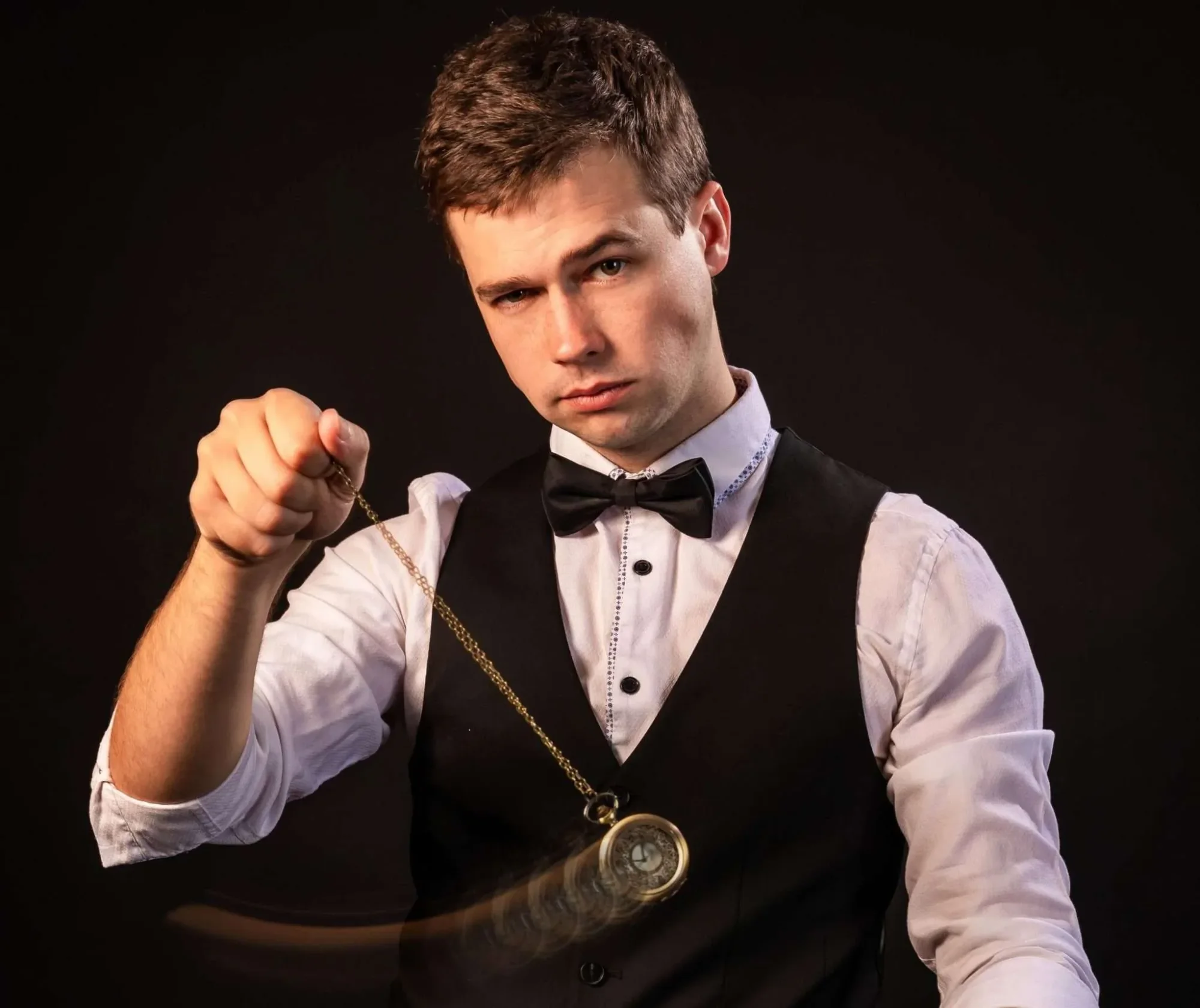 Magician in a tuxedo performing a hypnotic act with a pendulum