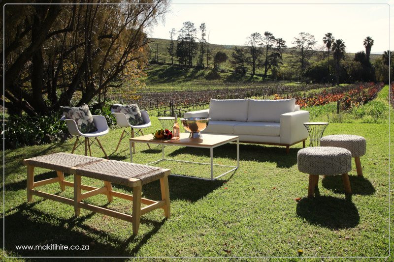Outdoor lounge setup with white couch and armchairs in a vineyard