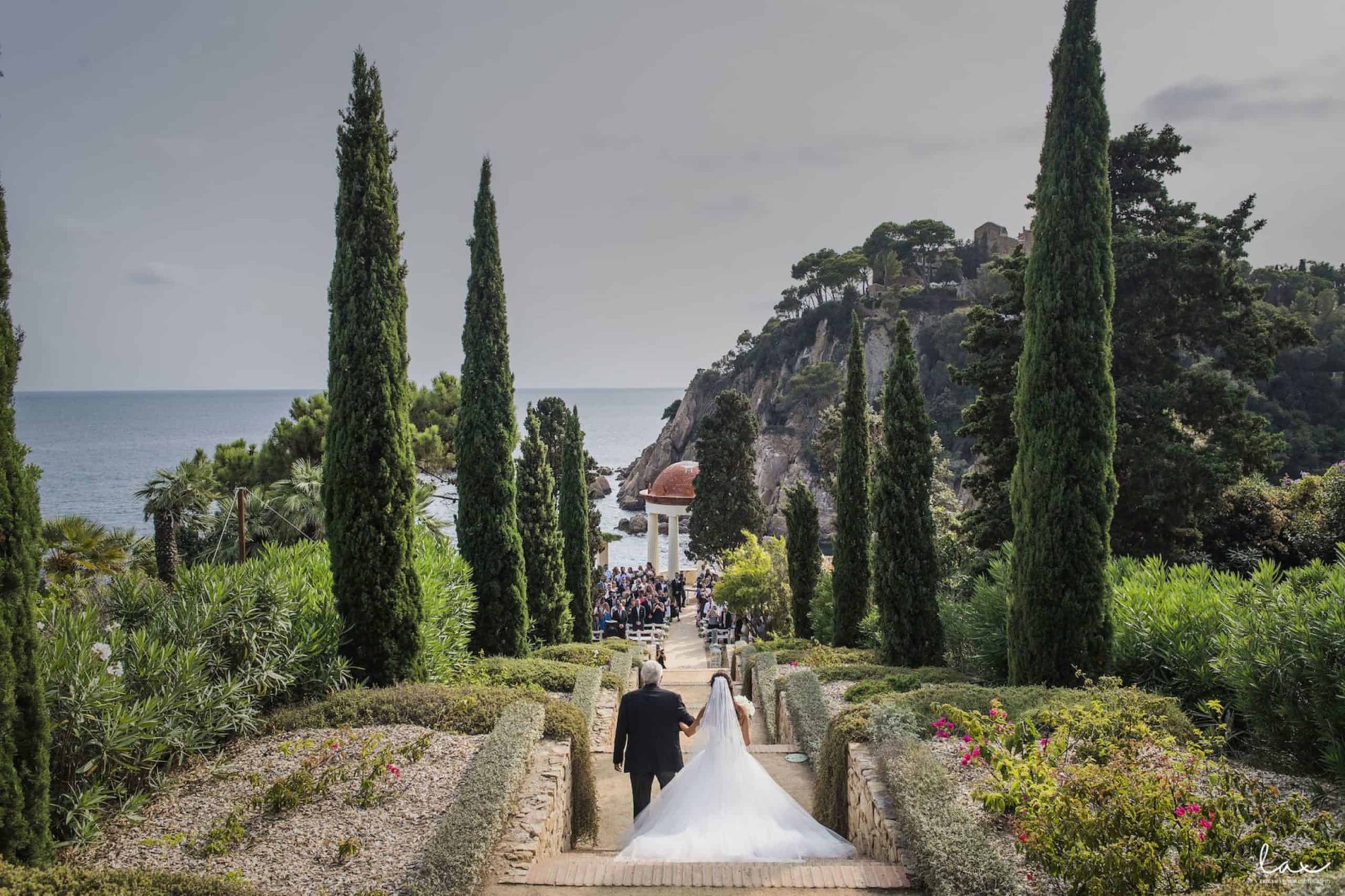 Couple walking towards a seaside wedding venue with beautiful greenery