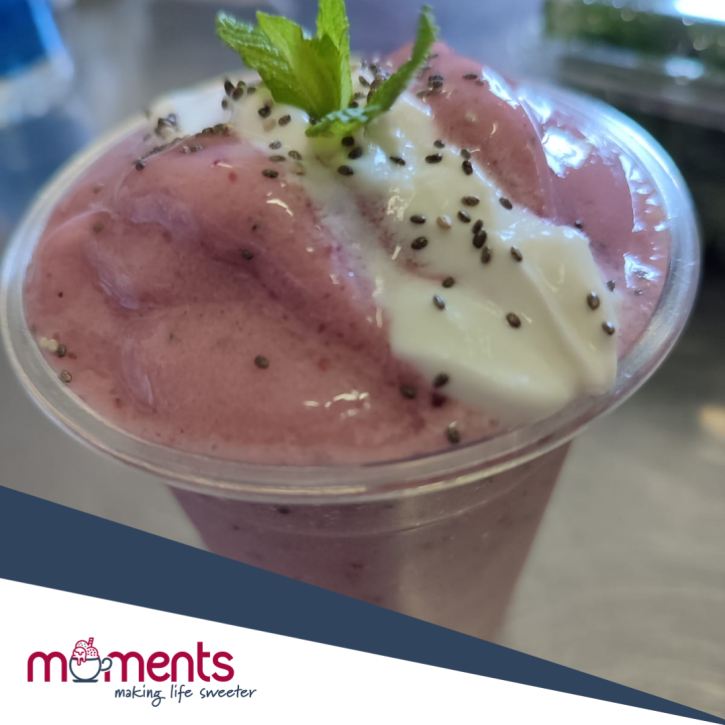 Berry smoothie topped with cream and mint leaf in a cup.