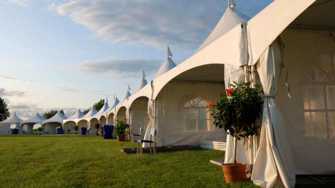 Row of marquee tents with flower pots on grass
