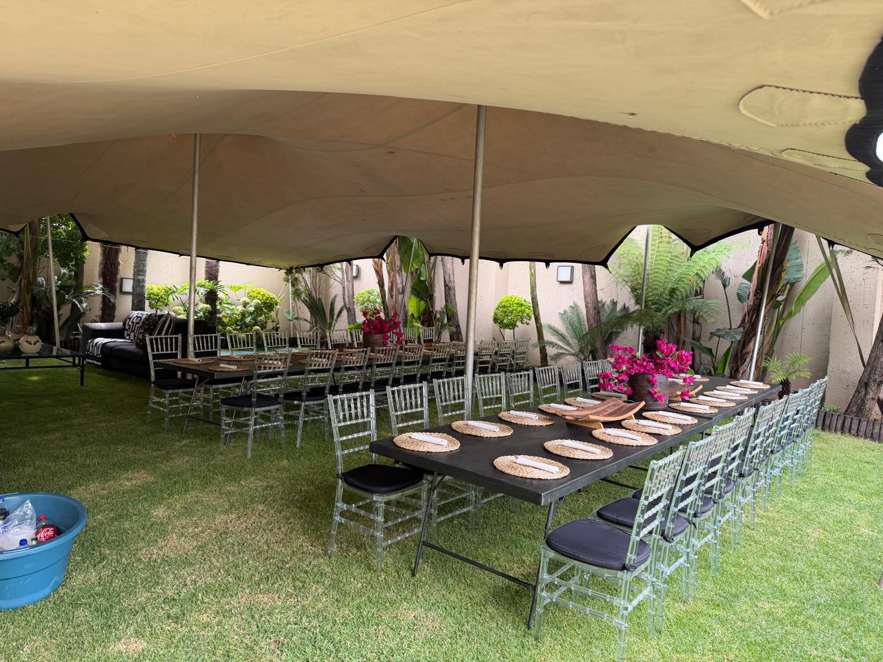 Outdoor dining setup with tables and chairs under a marquee.