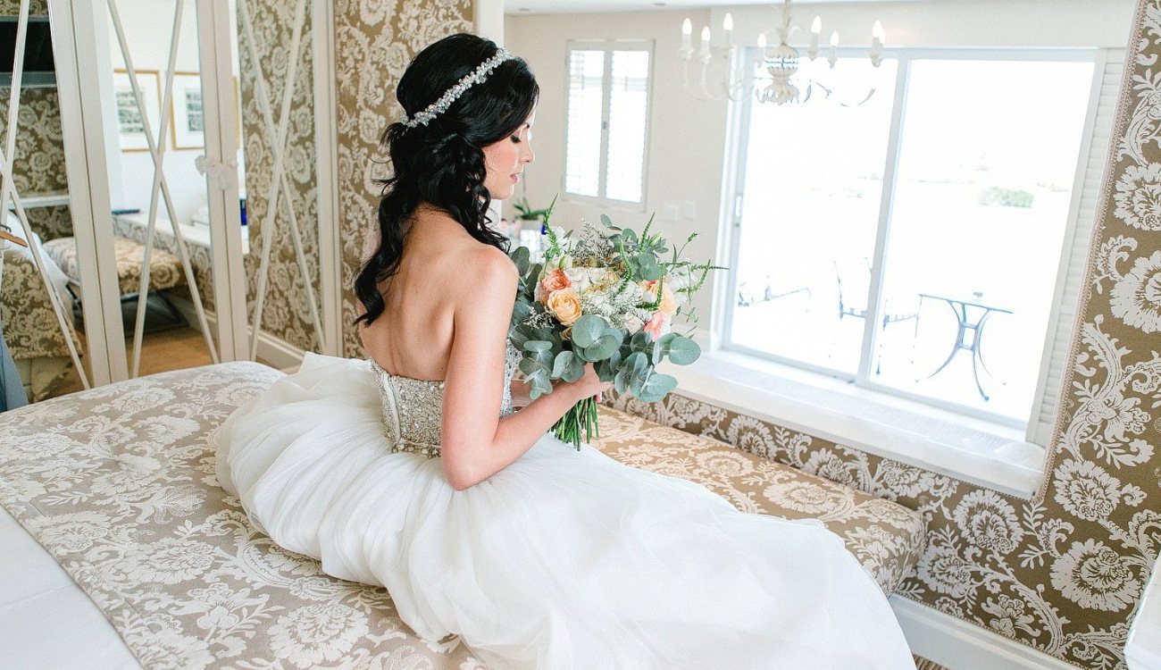 Bride sitting on a bed holding a floral bouquet
