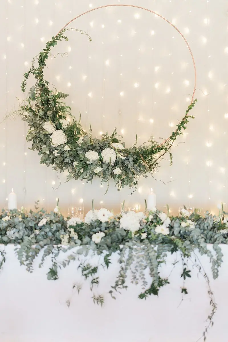 Hanging floral arrangement with greenery and white flowers against a lit backdrop.