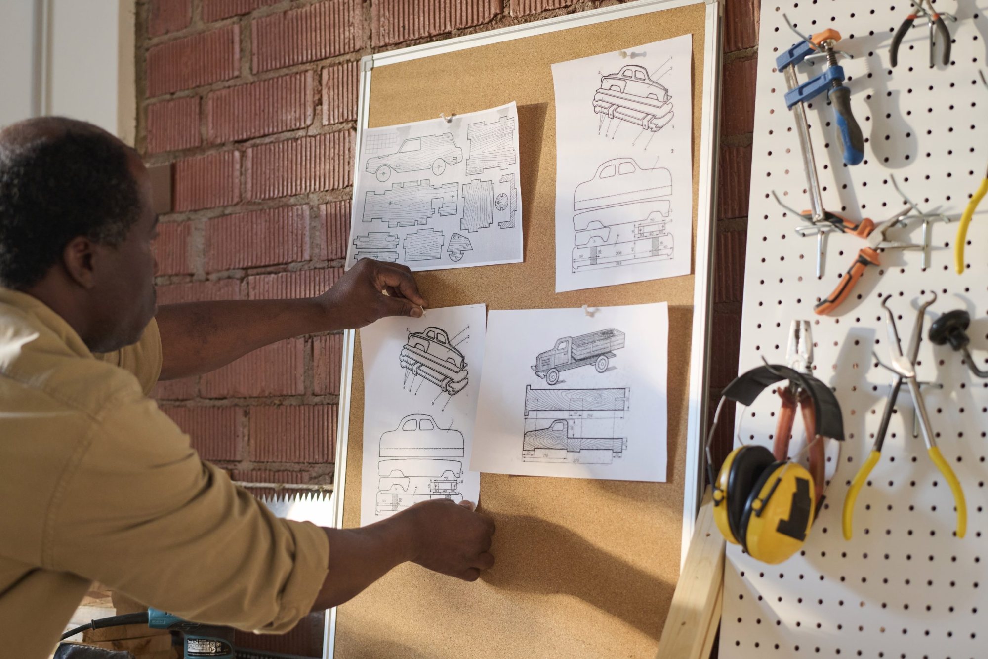 Man pinning sketches to a corkboard in a workshop