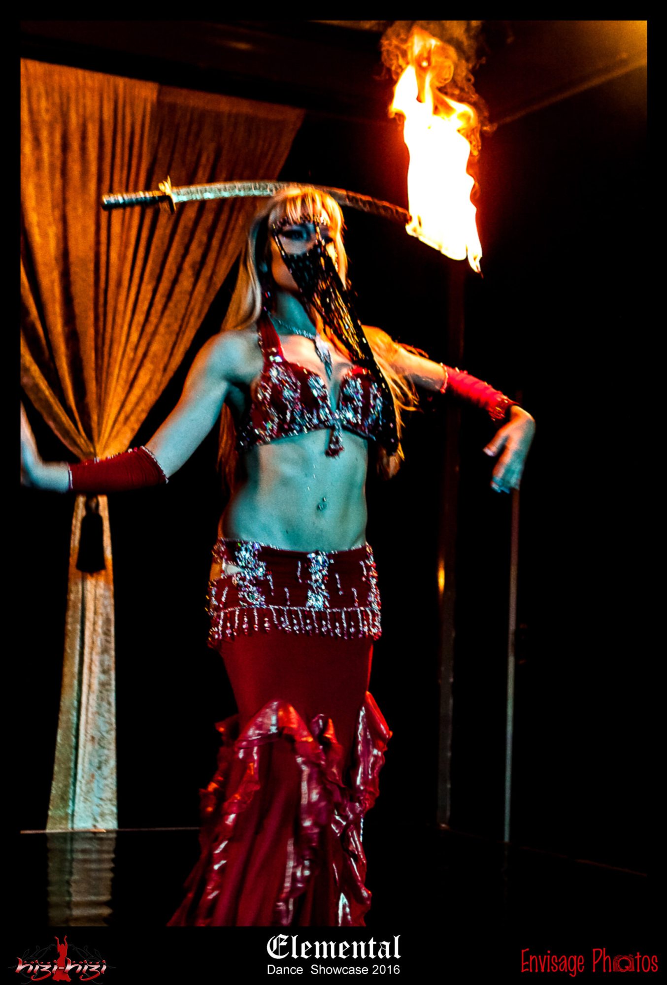 Belly dancer wielding a flaming sword in red attire.