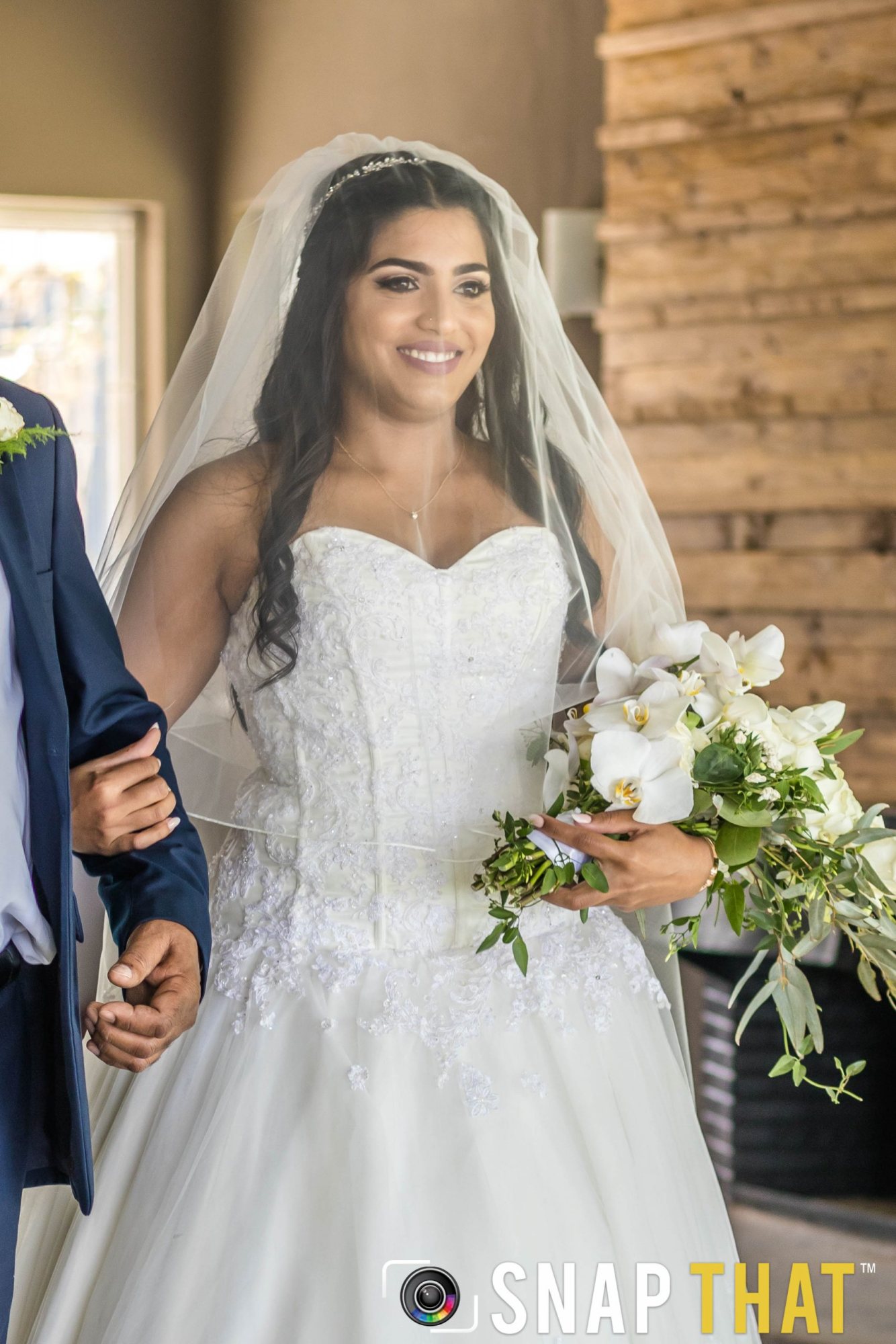 Bride in wedding dress with bouquet smiling as she walks down the aisle