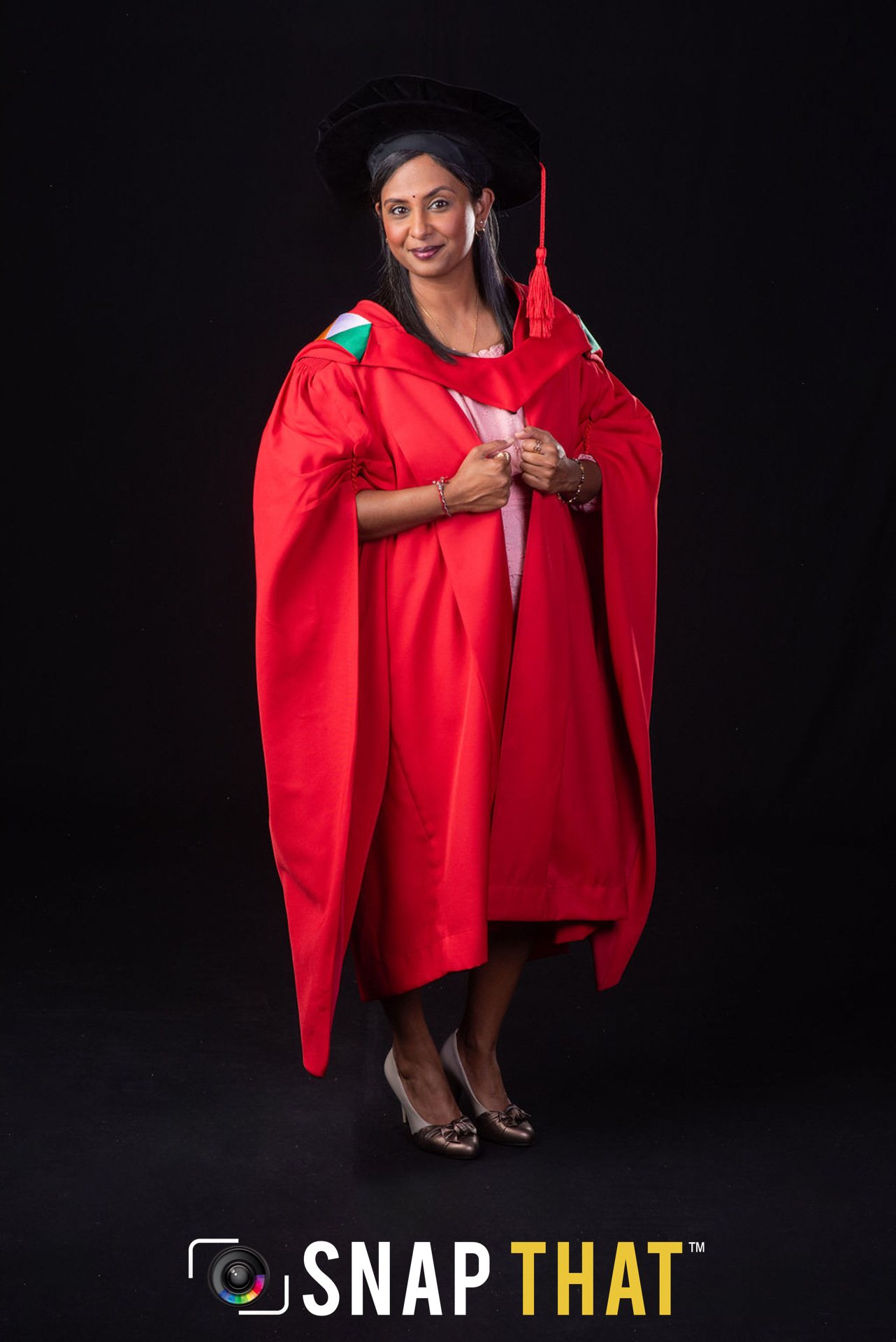 Graduate in red gown and hat posed against a dark background