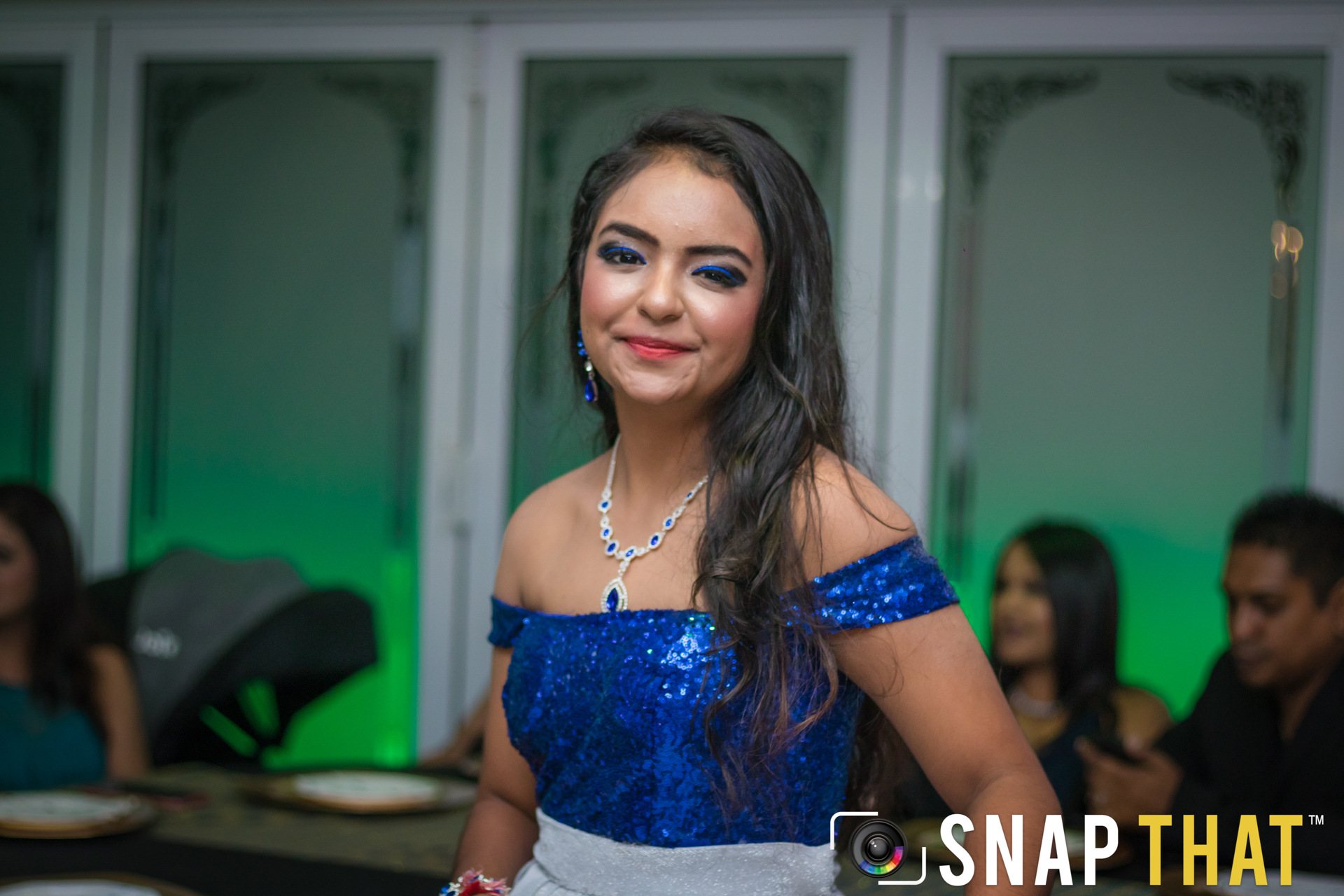 A young woman in a blue dress smiling at a celebration.