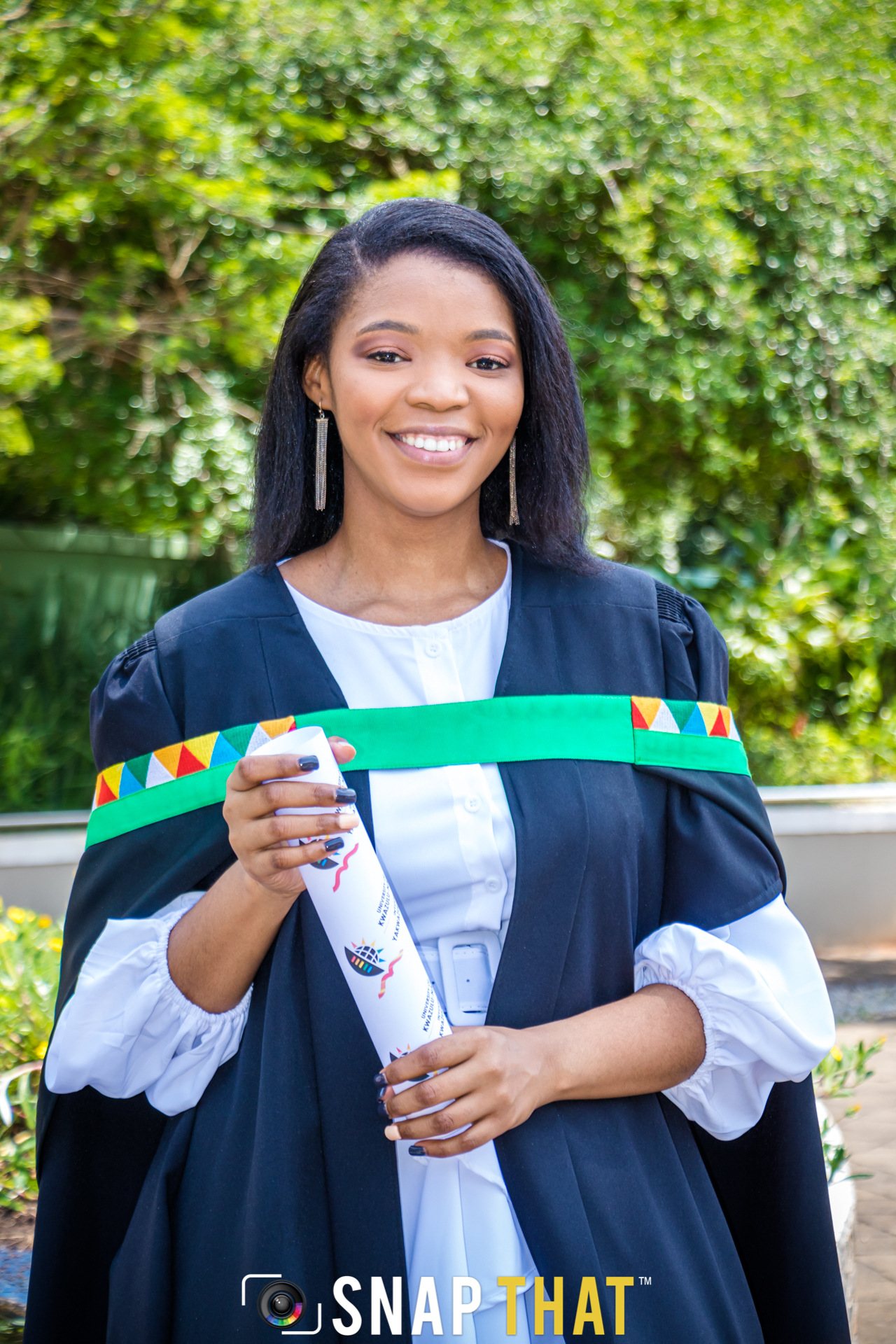 Smiling graduate holding a graduation scroll in academic attire.