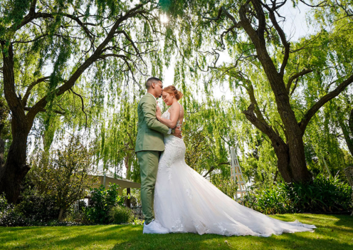 Bride and groom embracing under trees at an outdoor wedding