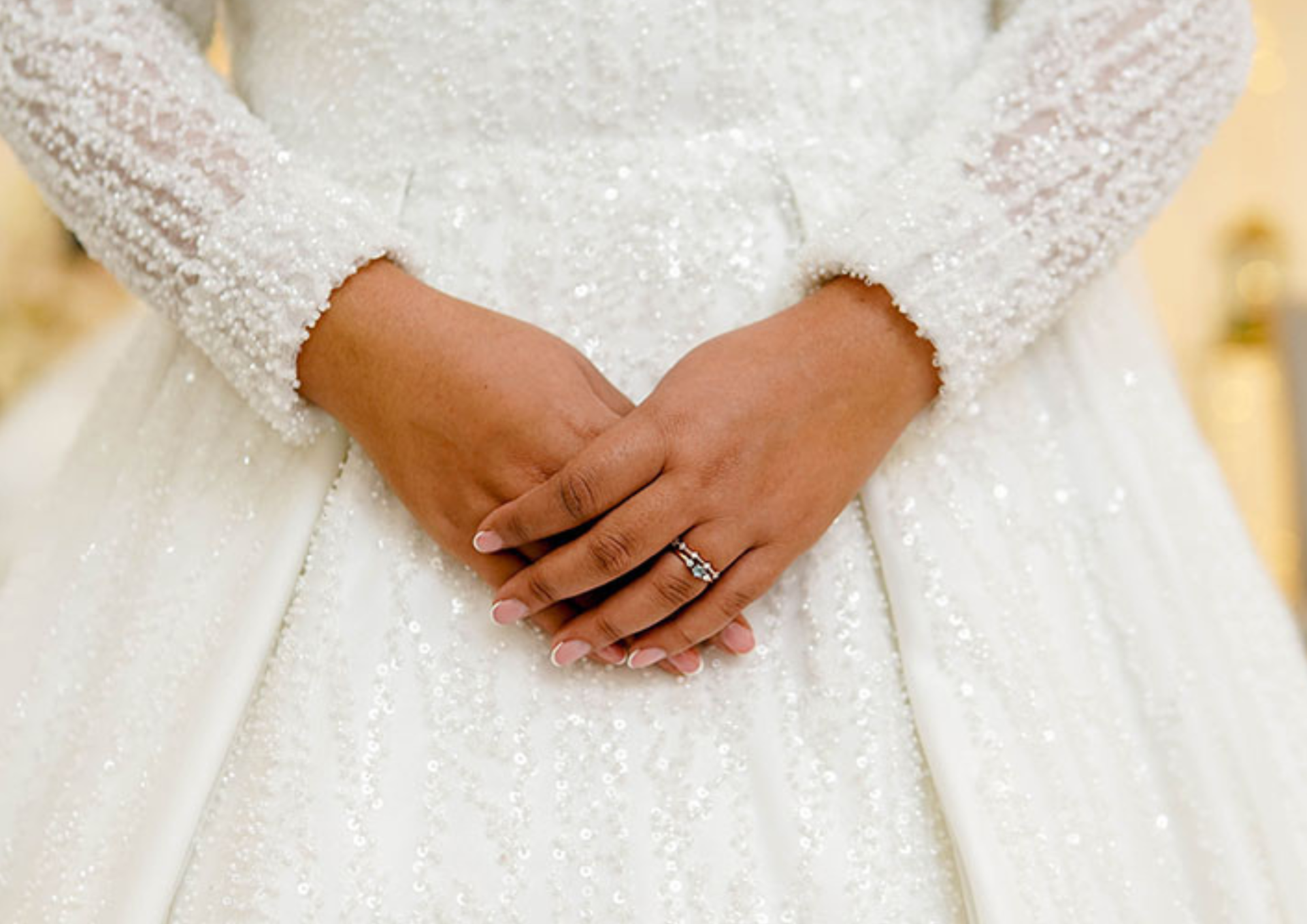 Close-up of a bride's hands with a ring on a gown