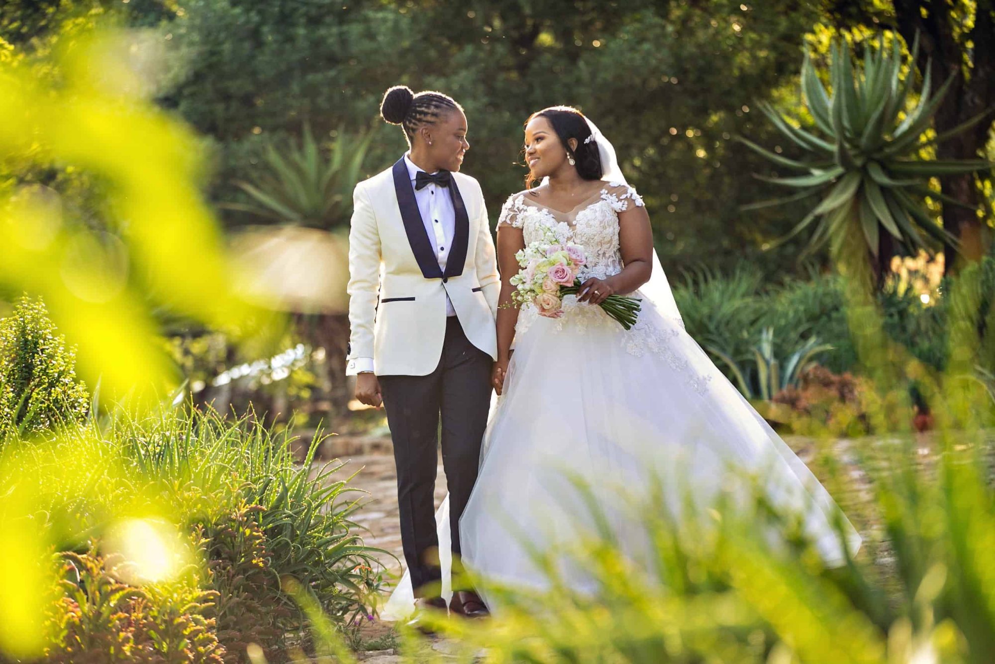 Two brides walking together in a garden setting.