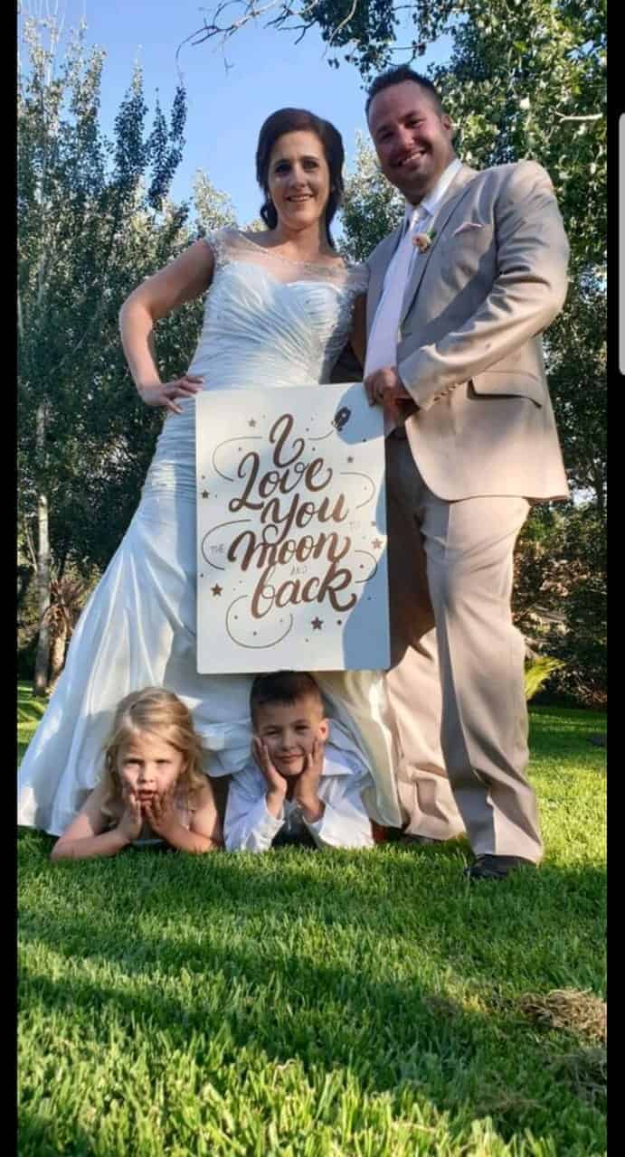 Couple in wedding attire holding a sign with children below them