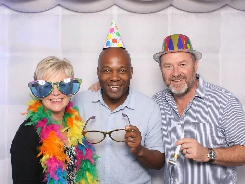 Three people in a photo booth with props and hats