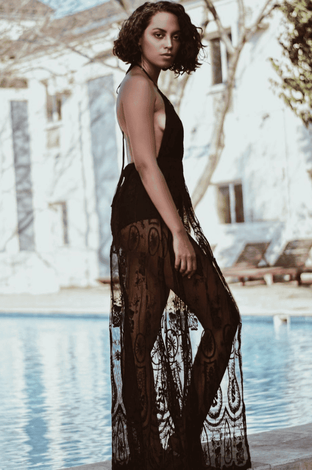 Model in a sheer black boho dress by a pool.