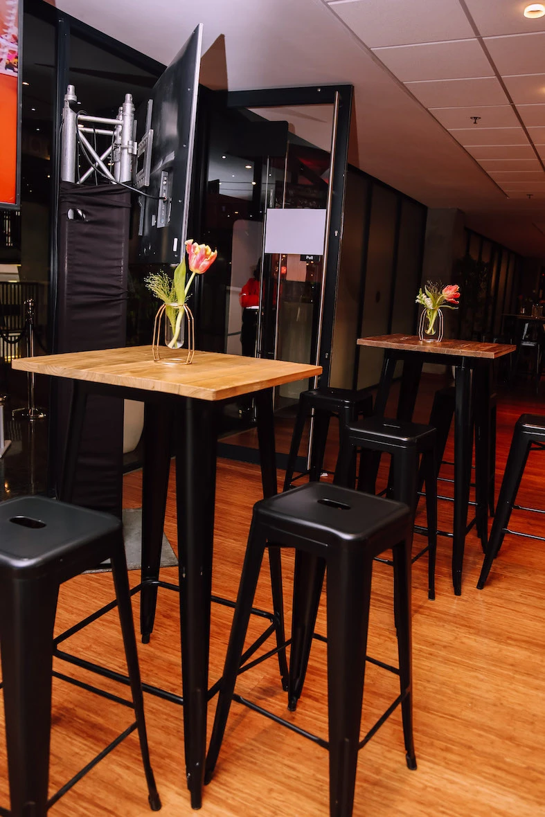 Set of black cocktail tables with wooden tops and flower vases.