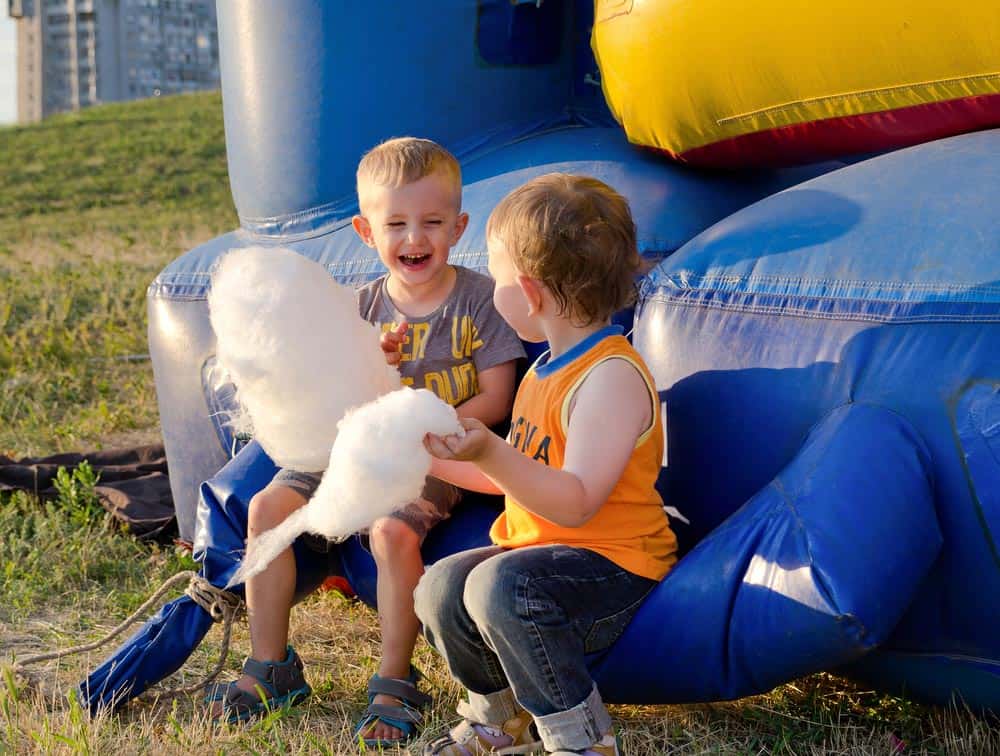 Two children sharing cotton candy near a bouncy castle.
